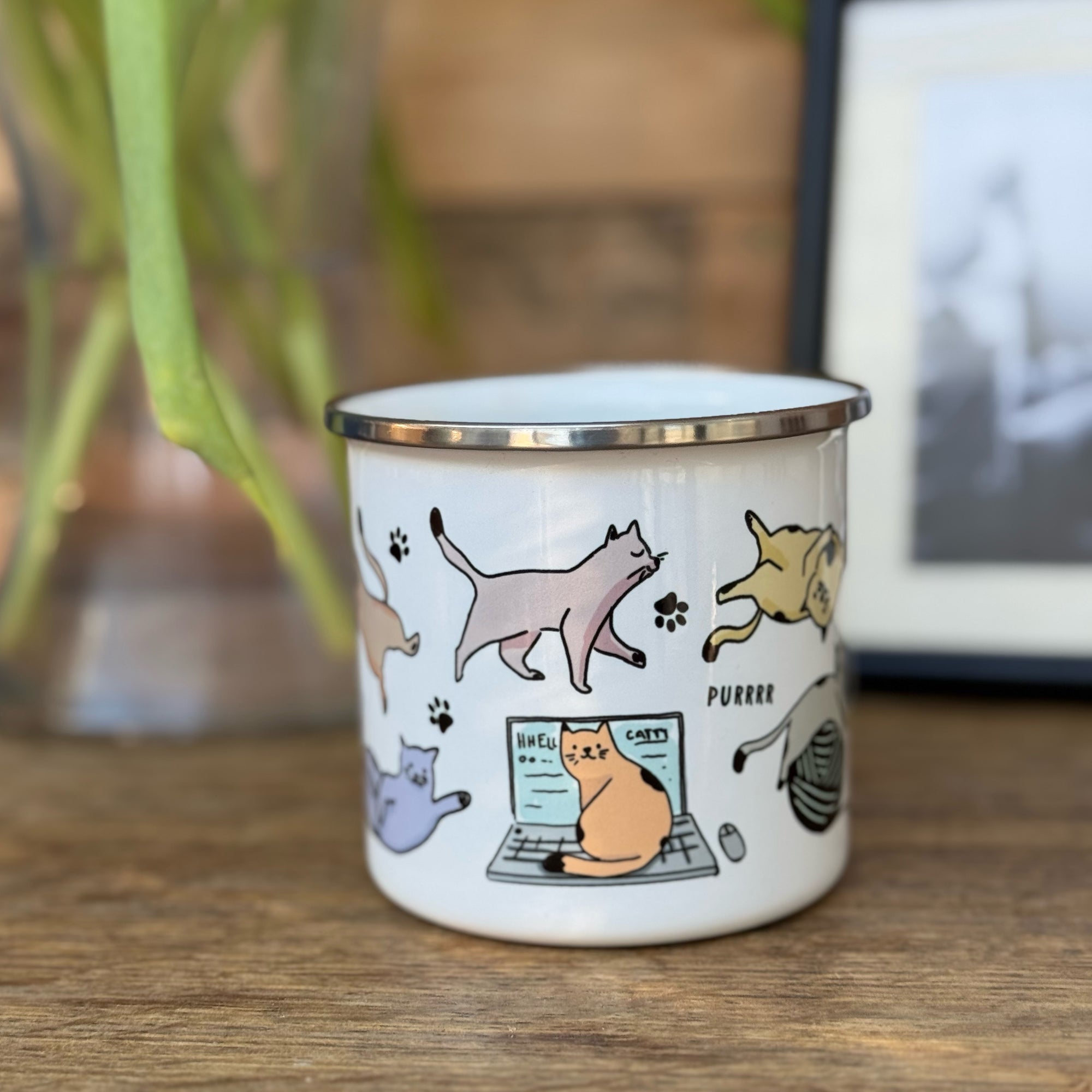 A colourful enamel mug with various cats and paw prints