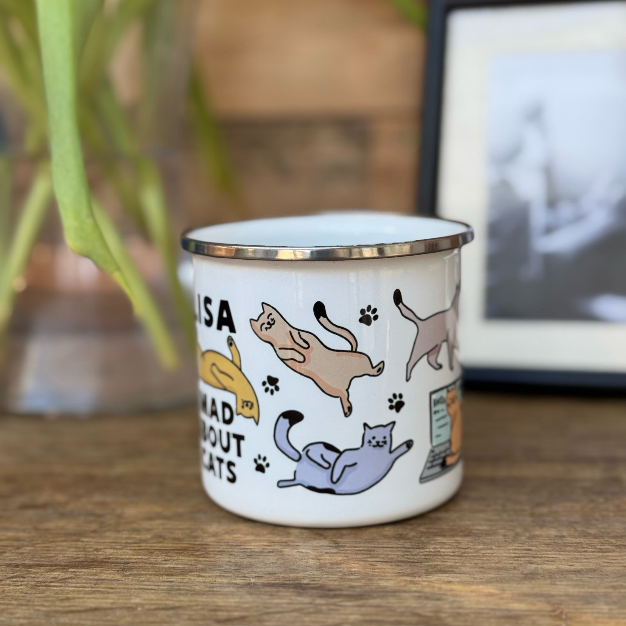 A tin mug with colourful wraparound cat designs With name & text 'Mad about Cats'