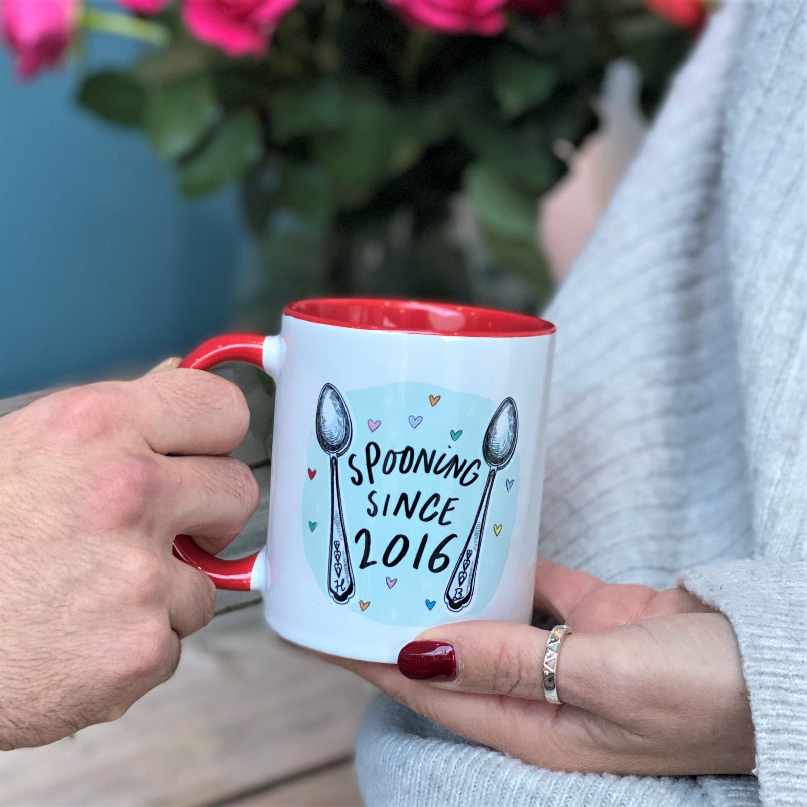 man giving lady a mug with spooning design for valentines with roses in the background